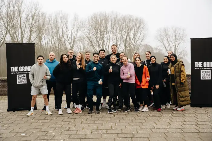 Eine Gruppe von Menschen posiert draußen für ein Gruppenfoto zwischen zwei Bannern mit Text und QR-Codes an einem winterlichen Tag.