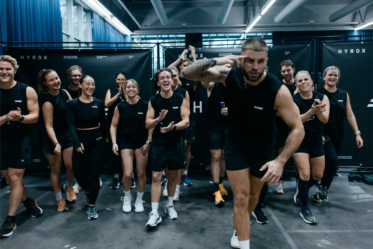 Gruppe sportlicher Männer und Frauen in schwarzer Sportbekleidung, die in einem Fitnessstudio lachen und applaudieren.